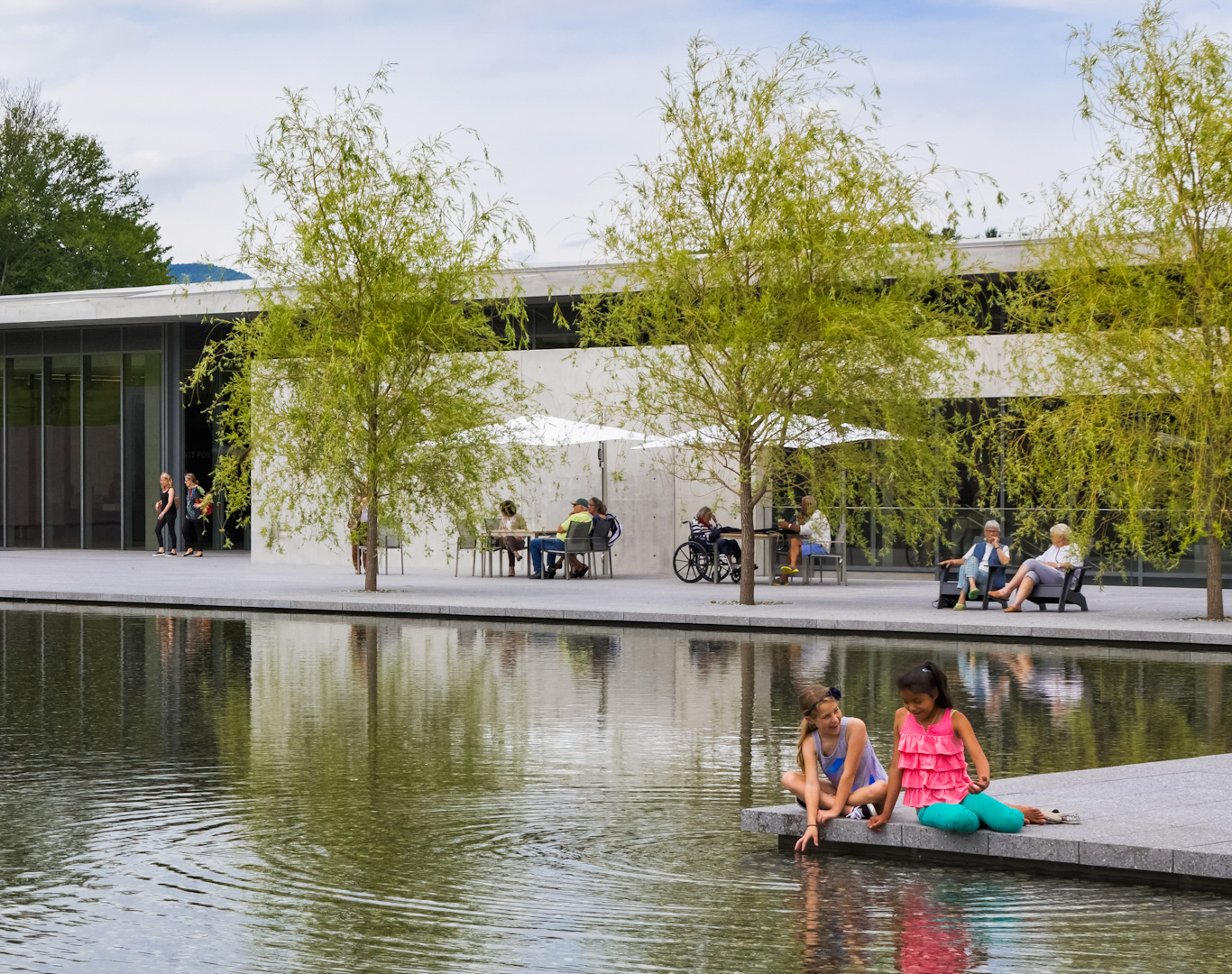 Multiple people of different ability levels sit on a patio in front of a reflecting pool